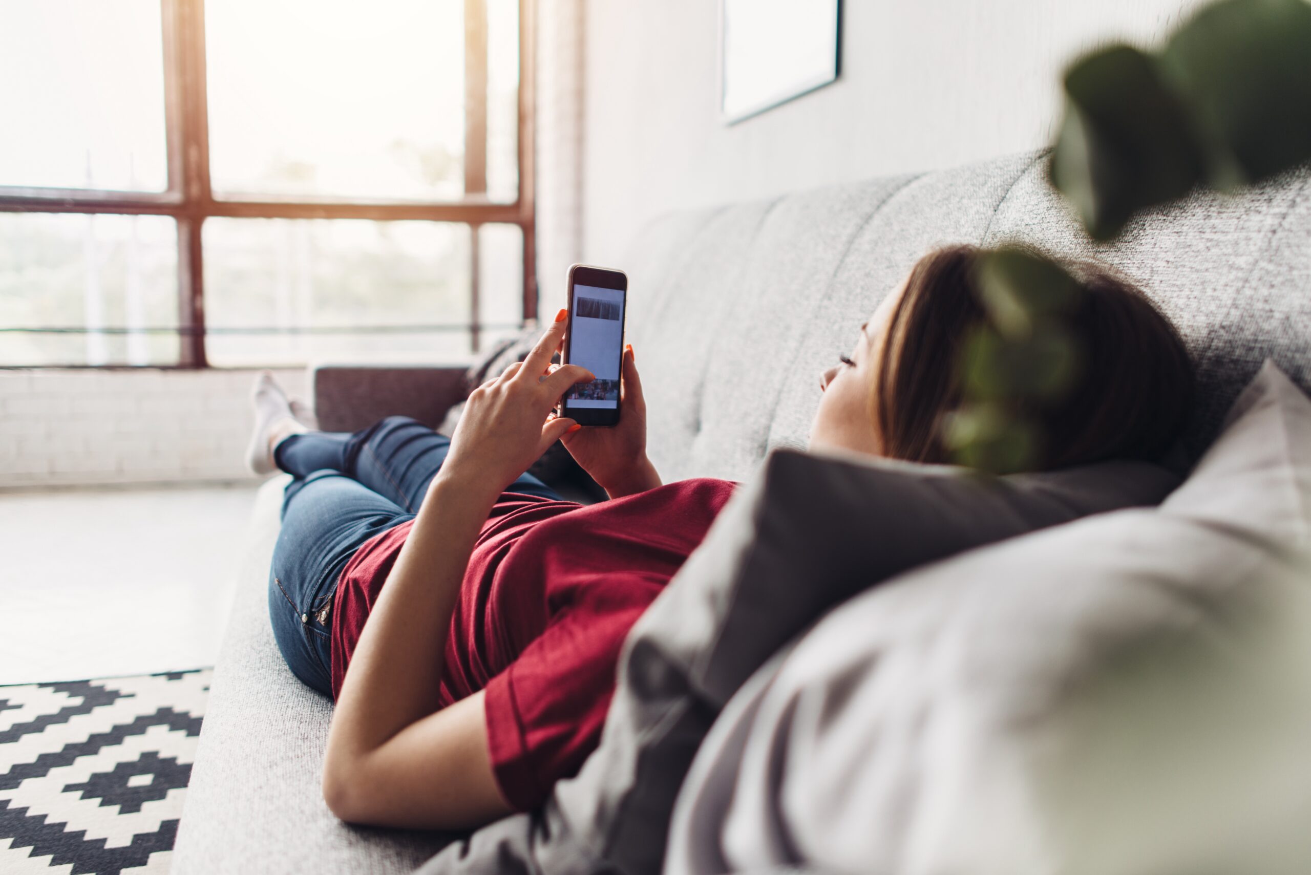 Young woman using smart phone while lying on the couch at home
